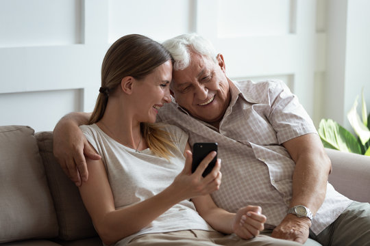 Happy young woman showing funny photos on smartphone to father.