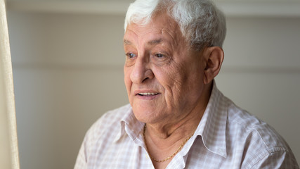 Happy older retired man looking with hope out of window.