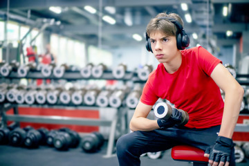 young man in sports clothes and headphones is engaged with dumbbells in the gym