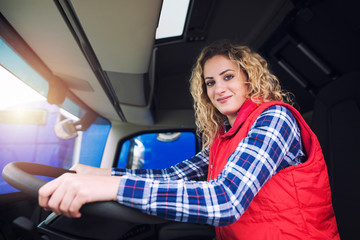 Truck driver occupation. Woman sitting inside truck at driver's position. Transportation service.