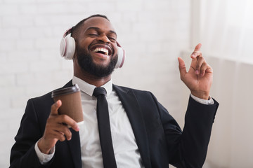 Joyful businessman singing, listening to music and drinking coffee