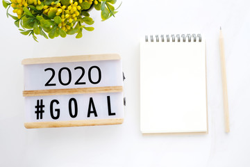 2020 goals on wood box and blank notebook paper on white marble background, business new year aim to success