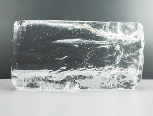 Large melting cube of clear ice on a white table and gray background. Clear Ice for sculpting