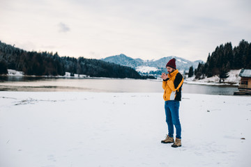 Young tourist arrived in amazing landscape place with big lake and forest , beside of a wooden house he have a little break with hot tea