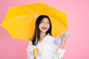 Asian teenager girl holding yellow umbrella during cold rainy day,drinks hot coffee to warm herself, pink background.  Autumn concept