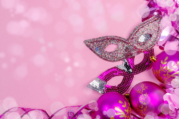 Christmas festive mockup. Frame of pink Christmas balls, tinsel, ribbon, carnival masks in pink background with bokeh. 
