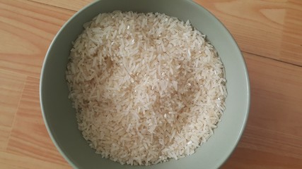 Top closeup view of heap of rice in a ceramic bowl placed over wooden floor