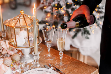 New Year 2020. New Year mood. Table with a gold tablecloth, decorated with candles and tableware for celebration. Festive still life by candlelight.A man pours champagne into a glass. Close-up.