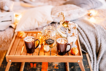 Table with a cup on the bed, marshmallow and Christmas cookies, cozy knitted blanket. New Year 2020, flat lay. Christmas composition with a cup tray and a mug