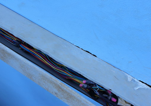 Closeup group of power lines inside broken electrical wireway installed on the wall of a building