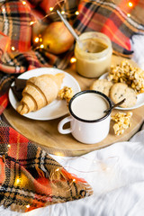 Simple country home breakfast in bed, coffee with milk and homemade pastry on plaid blanket