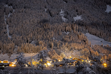 Winter night landscape with a view of the Austrian Tyrolean town of Neustift, in the background of fir trees in the snow