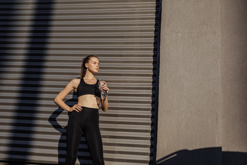 Fototapeta na wymiar Healthy female standing outdoors and drinking water after exercising session. Fitness woman taking a break after workout