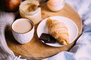 Cozy winter weekend breakfast, coffee and croissant on wooden tray