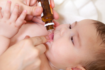 Medical drops oral vaccination to infant for immunisation. Mother holds glass bottle with liquid...