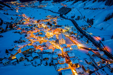 Winter night cityscape in the Austrian town of Neustift. Aerial view of the town center and the church. Night illumination of houses and traffic light. Tyrol, Stubai Valley