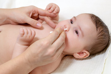Mother cleaning baby nose with cotton swab while infant lying on diaper board