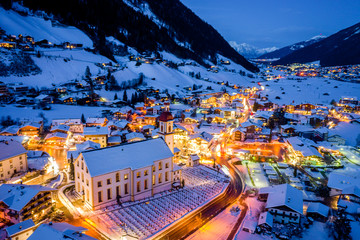 Winter night cityscape in the Austrian town of Neustift. Top view of the town center and the church. Night illumination of houses and traffic light. Tyrol, Stubai Valley - obrazy, fototapety, plakaty