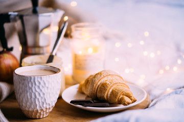 Cozy winter weekend breakfast, coffee and croissant on wooden tray