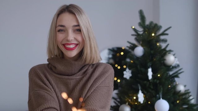 young blonde woman waving glow Christmas lights with bright splashes at home near christmas three
