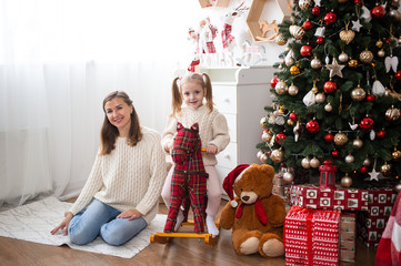Mother and little girl at home near Christmas tree and gift boxes