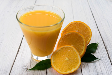 A glass of orange juice and slices of orange on a white wooden table.