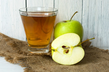 A glass of apple juice and a green apple on a white wooden background.