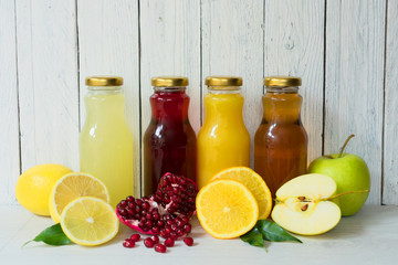 Four types of juice (pomegranate, apple, lemon, orange juice) in glass bottles on a white wooden background.