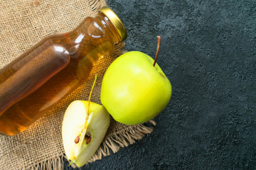  Apple juice in a bottle and a green apple on a black background. Flat lay. Copy space.