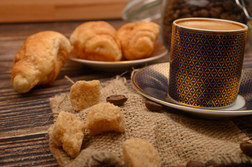 A Cup of coffee, brown sugar, croissants on a wooden background. Close up.
