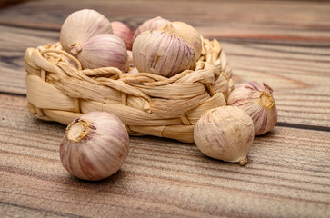 A few heads of young garlic in a wicker basket on a wooden background. Autumn harvest. Modern agriculture. Close up.