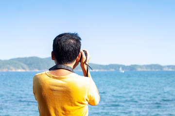 Male tourists stand to take pictures of the sea and mountains in the heat of the sun.