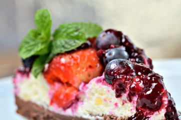Close-up of delicious fruit strawberry and blueberry cream cake glazed by cherry sauce and fresh mint leaves on decorative white plate. Low depth of field.