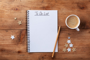 Naklejka na ściany i meble Cup of coffee, stars confetti and notebook with to do list on wooden table top view, Christmas planning concept. Flat lay style.