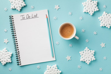 Cup of coffee, decorative snowflakes and notebook with to do list on turquoise background top view,...