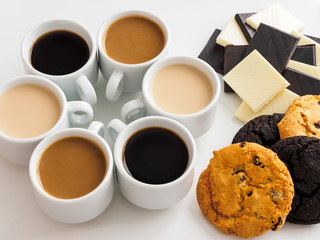Several types of coffee in white cups. Lots of different sweets. Family coffee party