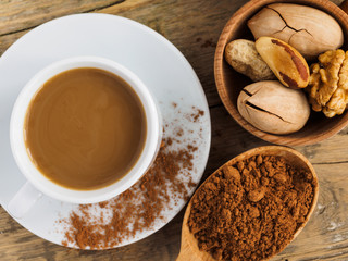 Coffee in a white Cup, nuts and cocoa in a spoon on a wooden table