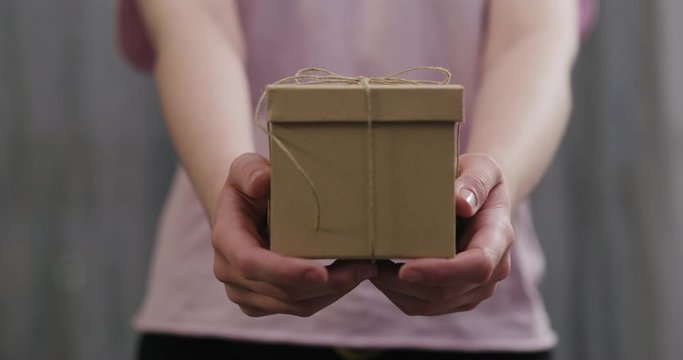 Slow motion young woman stand and show brown gift box with twine bow