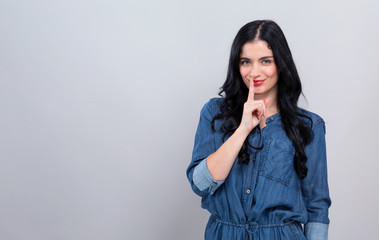 Young woman making a quiet gesture on a gray background