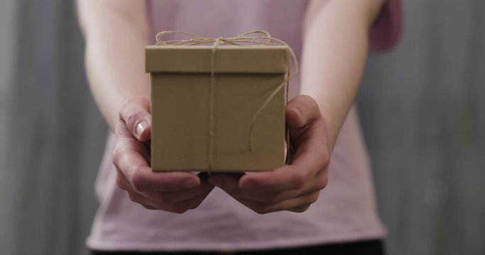 Slow motion young woman stand and show brown gift box with twine bow