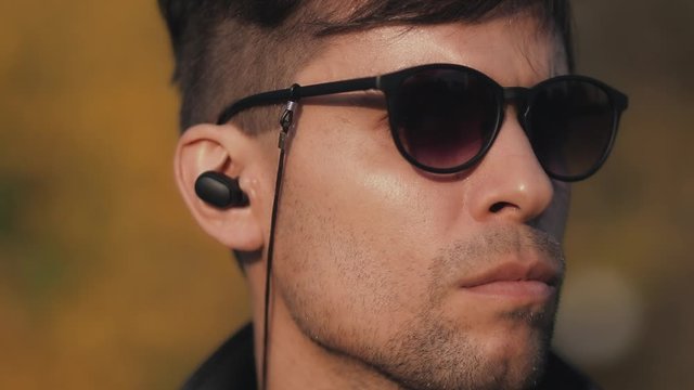 Close-up of a man's face with blurred background in sunglasses with wireless headphones