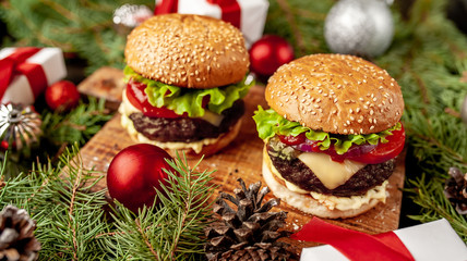 Christmas dinner for two, two homemade hamburgers with salad and cheese on a stone table with a Christmas tree and Christmas toys