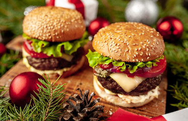 Christmas dinner for two, two homemade hamburgers with salad and cheese on a stone table with a Christmas tree and Christmas toys