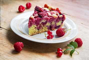 Still-life a piece of berry pie on a plate, raspberry, red currant, a leaf on a wooden board with a shallow depth of field