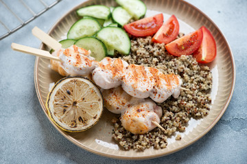 Chicken skewers with quinoa, tomatoes, cucumber and lemon served on a beige plate, studio shot