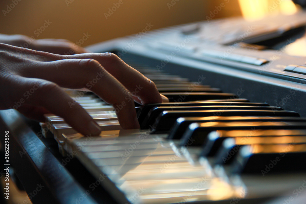 Wall mural Details of a hand playing on keyboard under a smooth light