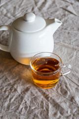 White teapot with glass cup with tea on table