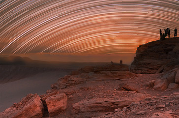 Young people is on the rock. Night glowing stars trails in the sky.  Long exposure