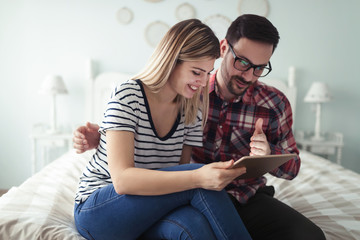 Happy couple using digital tablet in bedroom