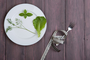 Dieting concept - white plate with dill, salad lettuce, basil, fork and centimeter tape